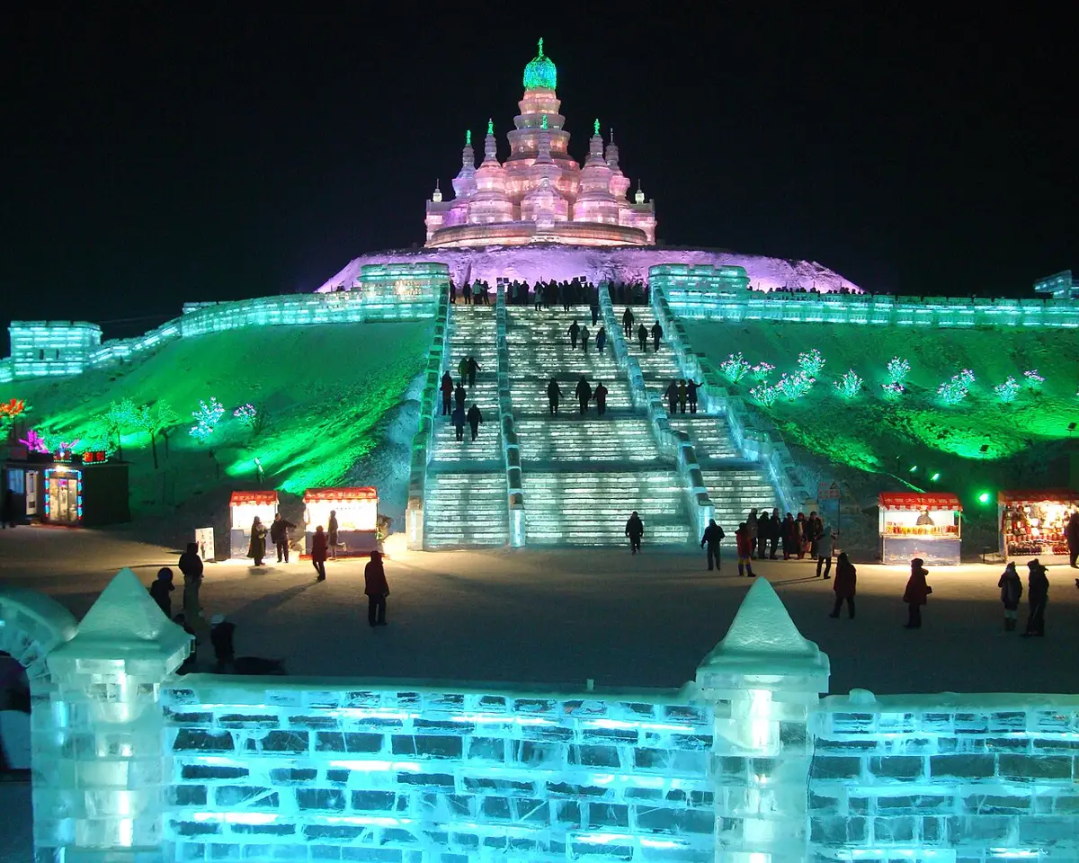 Imagem do Festival de Gelo de Harbin, na China, com esculturas de gelo iluminadas por luzes coloridas, criando um cenário mágico.