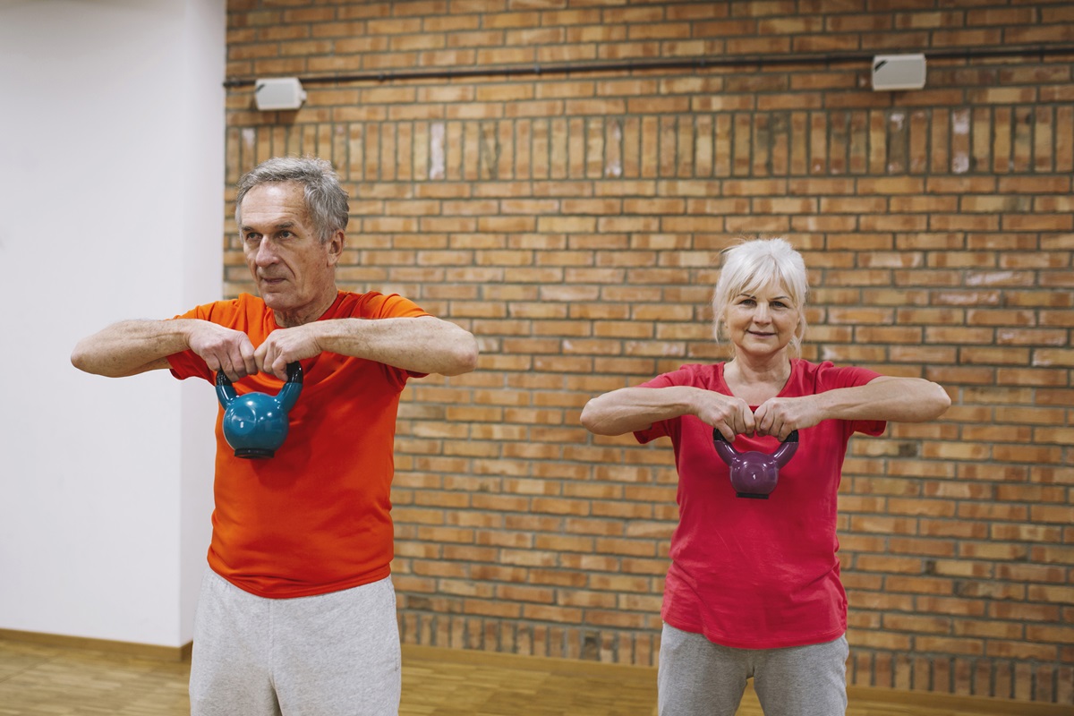 Casal de idosos treinando com kettlebells em uma academia, praticando exercício físico de forma saudável