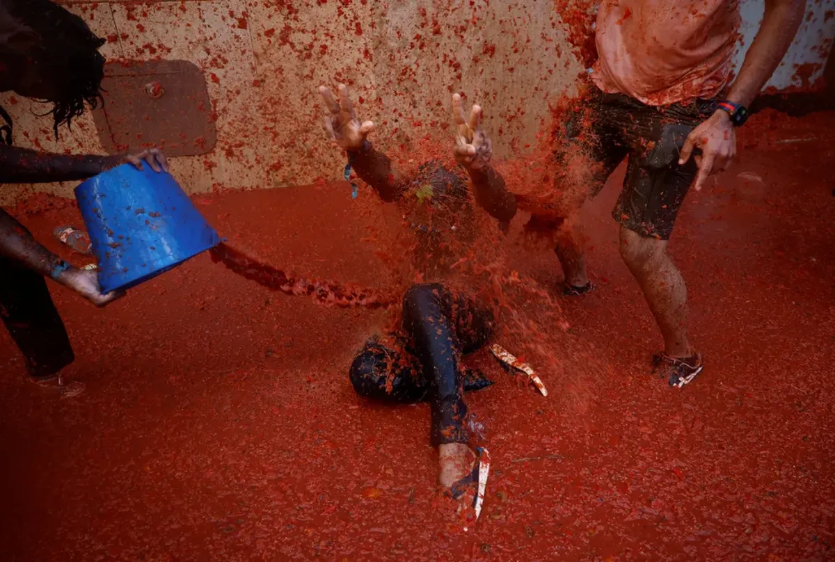 Participantes da La Tomatina se divertindo durante a maior batalha de tomates do mundo, com tomates espalhados pelo chão e pessoas se jogando.