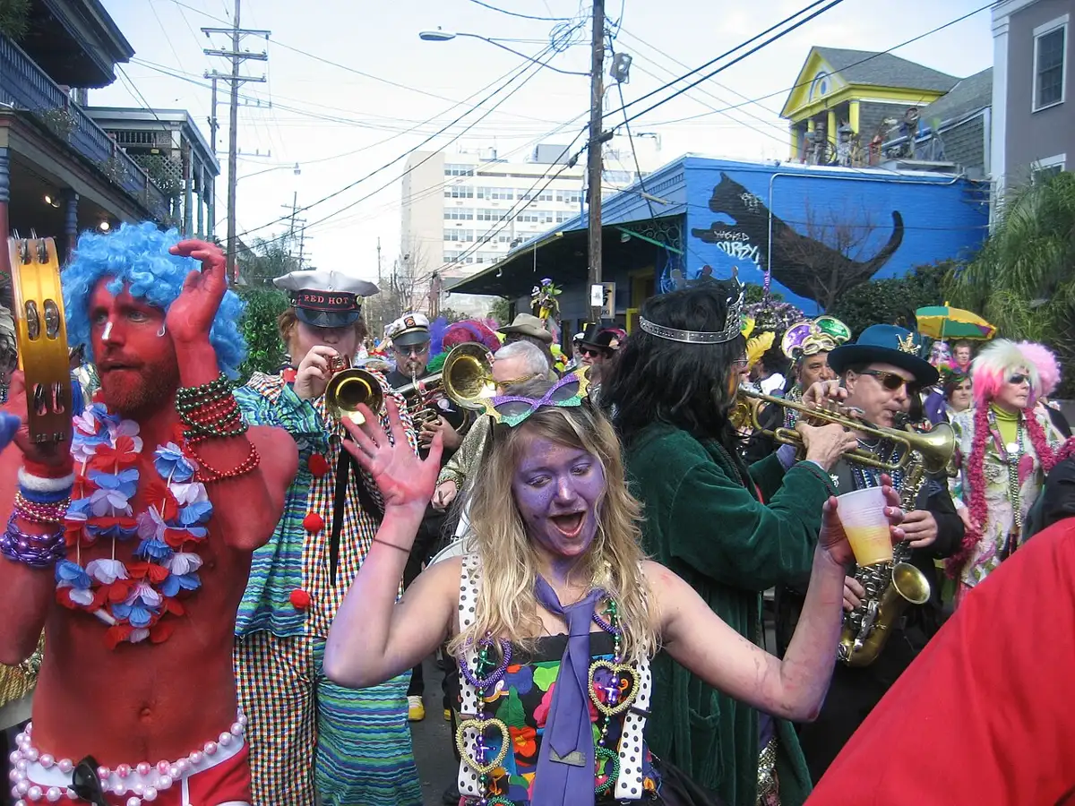 Festa de Mardi Gras em Nova Orleans, com foliões vestidos de maneira colorida e extravagante dançando e tocando instrumentos musicais durante o desfile.