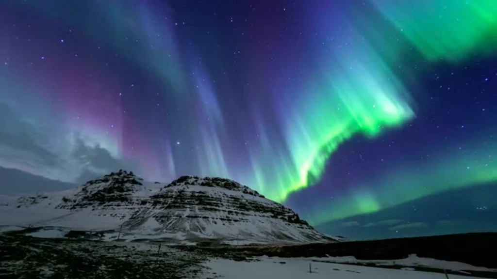 Luzes verdes e roxas da aurora boreal iluminando o céu noturno sobre uma montanha nevada