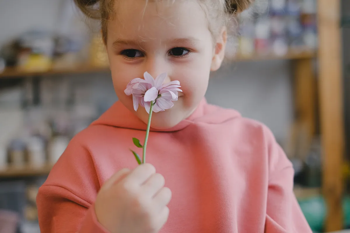 Criança sorrindo enquanto cheira uma flor, com uma expressão alegre e adorável.
