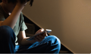 Jovem sentado com expressão preocupada olhando para o celular, ilustrando o impacto negativo das redes sociais
