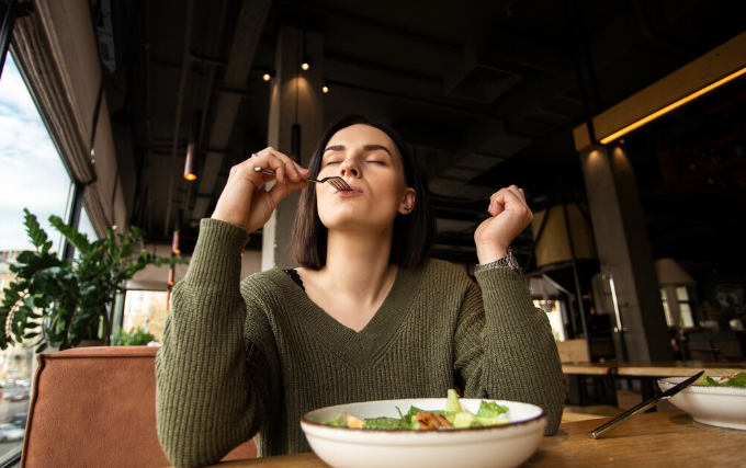 Mulher comendo e desfrutando de uma refeição saudável, ilustrando o aumento da fome no frio.