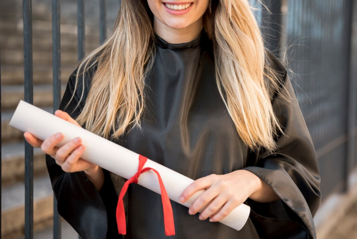 Jovem formanda com diploma de papel nas mãos sorrindo após a colação